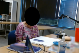 Image of participant wearing a pink shirt sitting in a user testing lab with materials including an insulin pump and an instruction manual on the table in front of her.