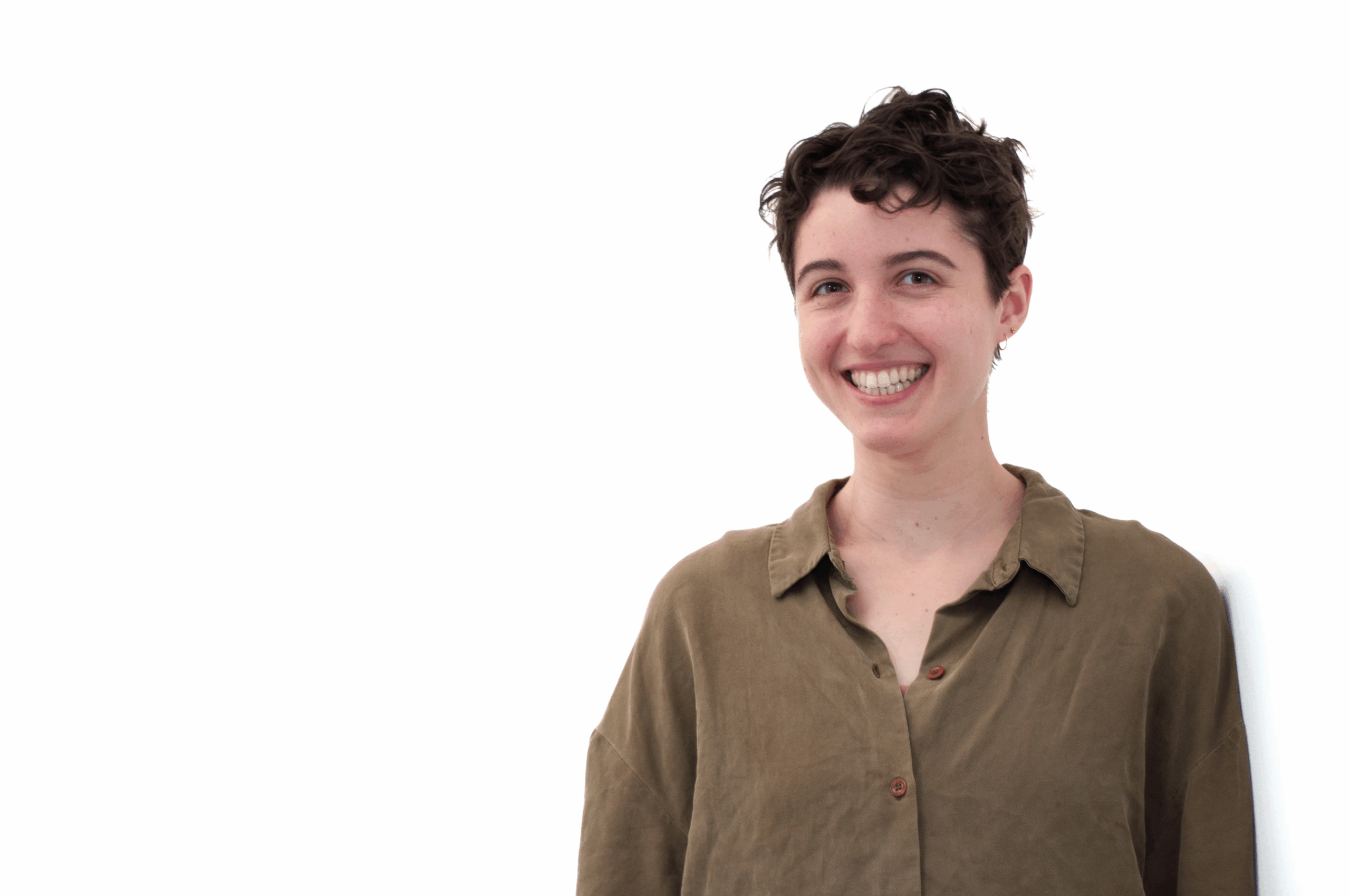 Caroline is smiling in a professional headshot on a white background. Caroline is white with short brown curly hair, and is wearing an olive green button-up shirt.