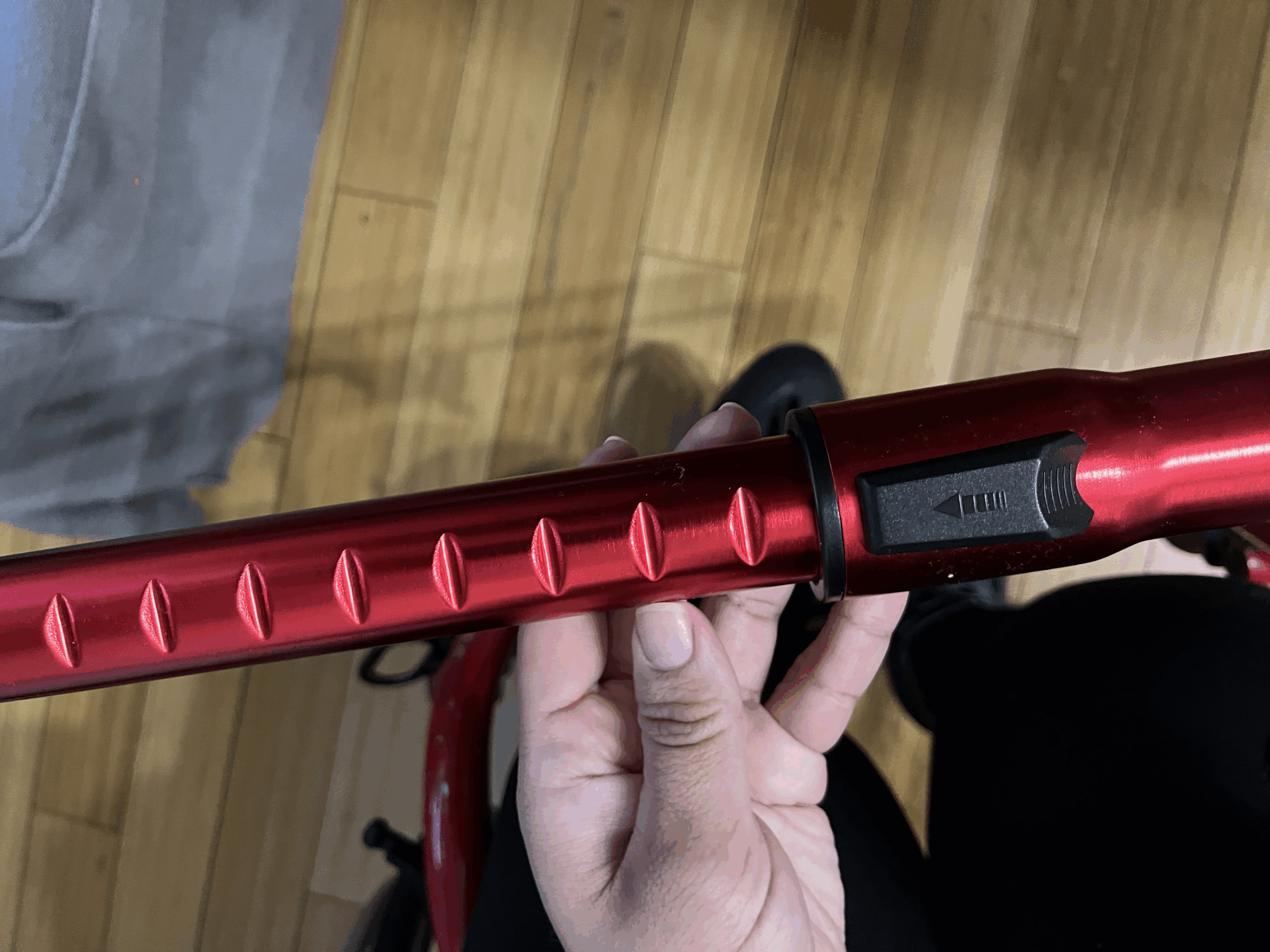 Photograph of a hand holding a metal red vacuum hose nozzle. The nozzle has notches to change the length and appears to be extended to the longest length possible.